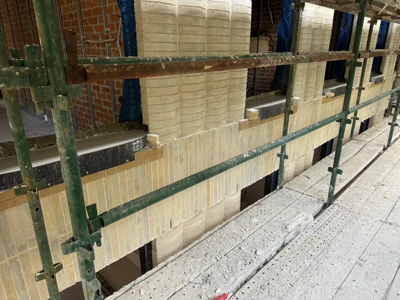 A run of curved window sills and travertine spandrel panels along the building, mid-construction