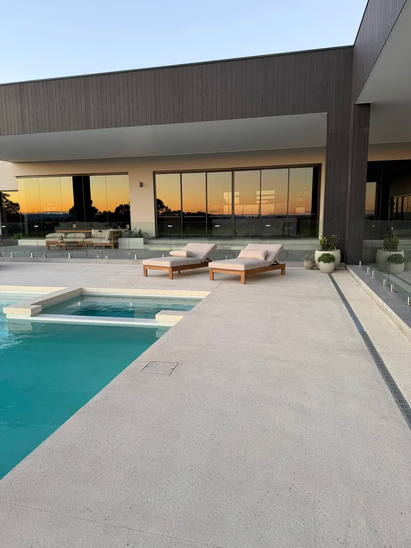 Close view of the exposed aggregate finish along the pool edge and the strip drain against the house