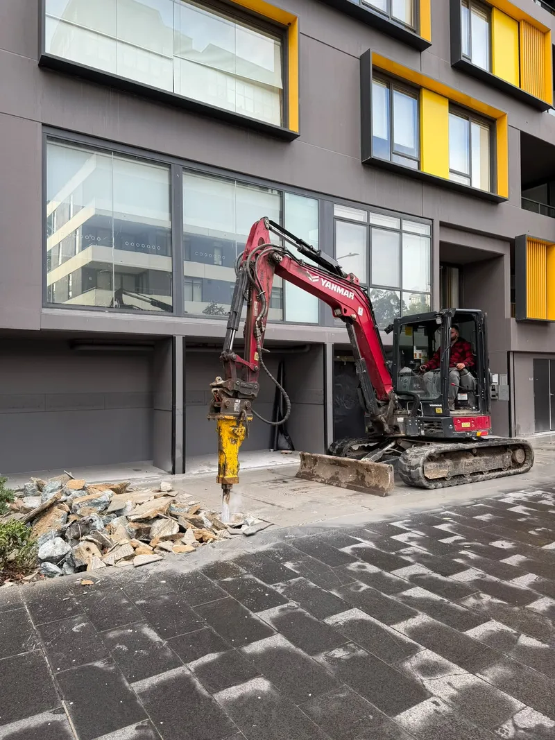 Excavator with a rock breaker attachment removing the old cracked tiles at the building entrance in Meadowbank