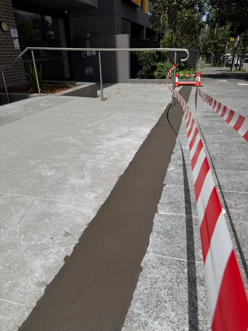 Close view of the freshly poured charcoal concrete entrance strip, taped off to cure