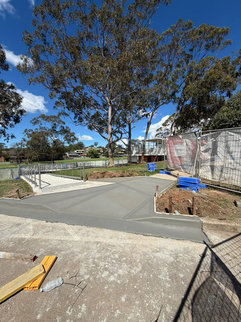 The finished broomed concrete apron meeting the curved white guard rail near the clubhouse
