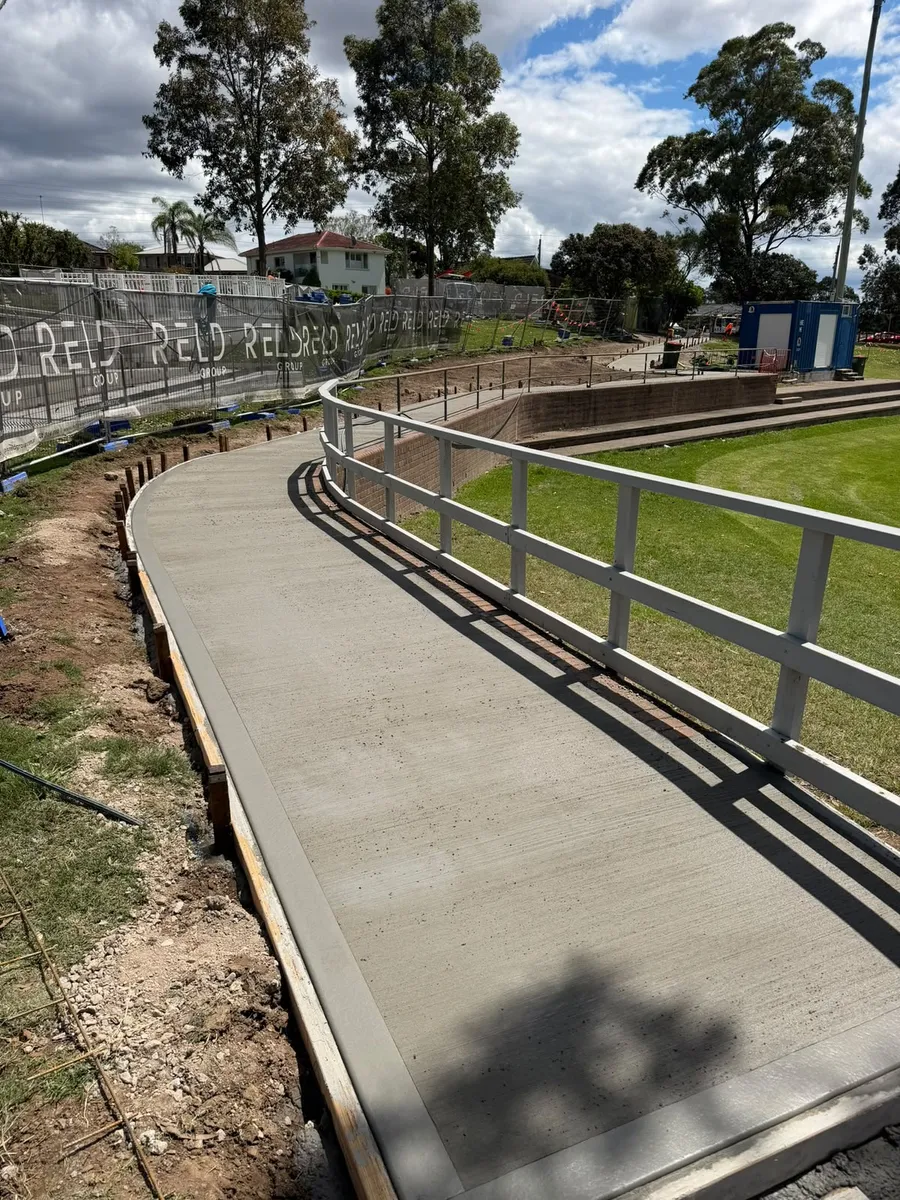 The finished curved broomed-concrete footpath along the oval at Max Ruddock Reserve, Winston Hills, with its white guard rail